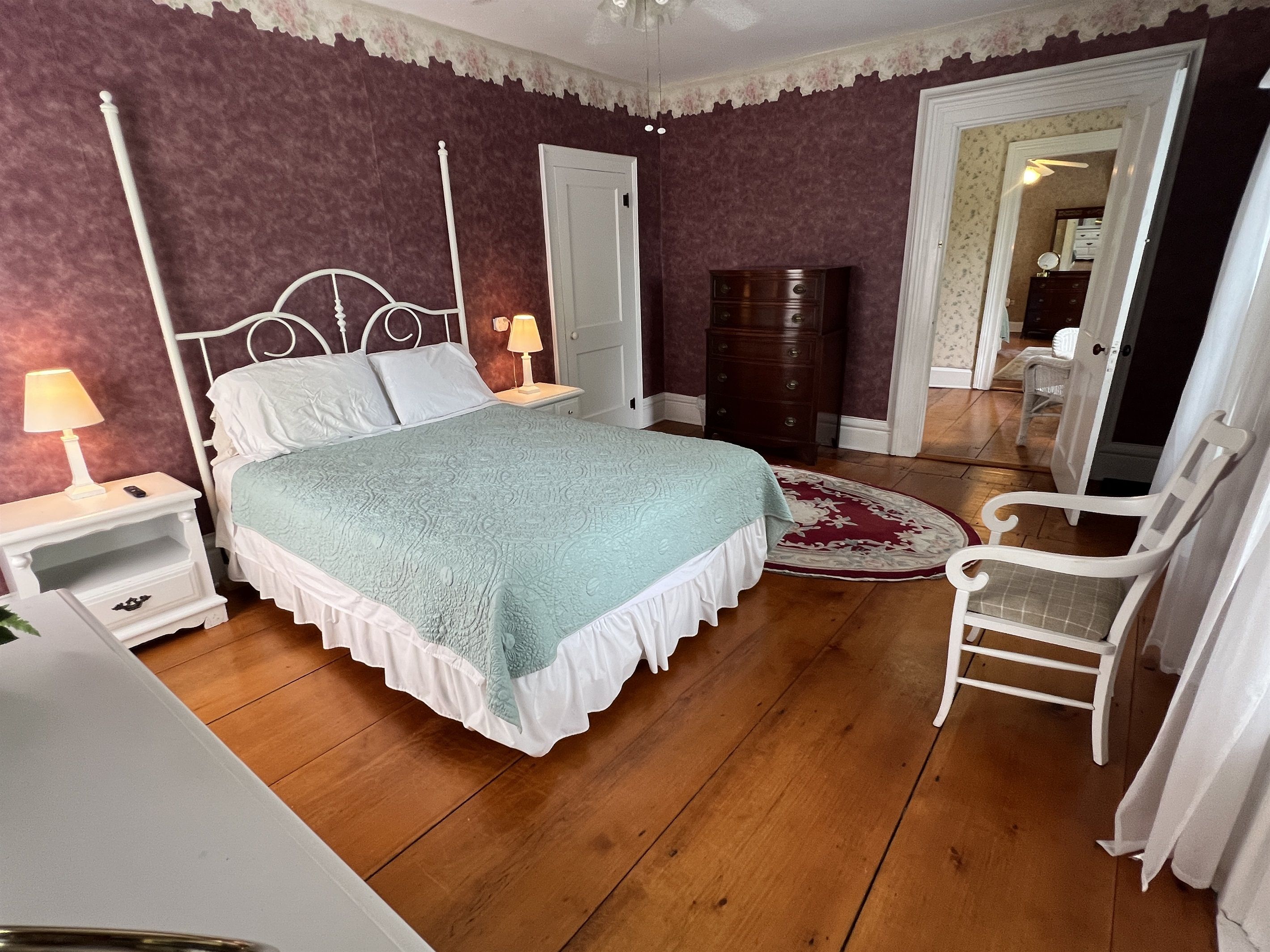 A bedroom with a four-poster bed, a nightstand with a lamp, a dresser, and a chair.