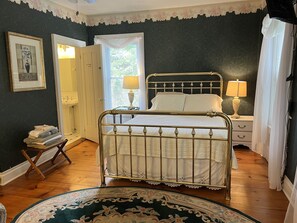 A bedroom with a metal-framed bed, a bedside table with a lamp, a nightstand, a mirror, a door, and a rug.