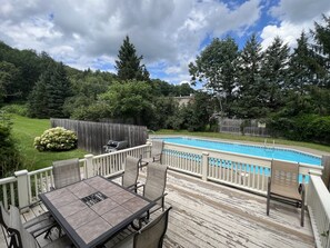 A backyard with a pool, a dining area with chairs and a table, and a wooden deck.