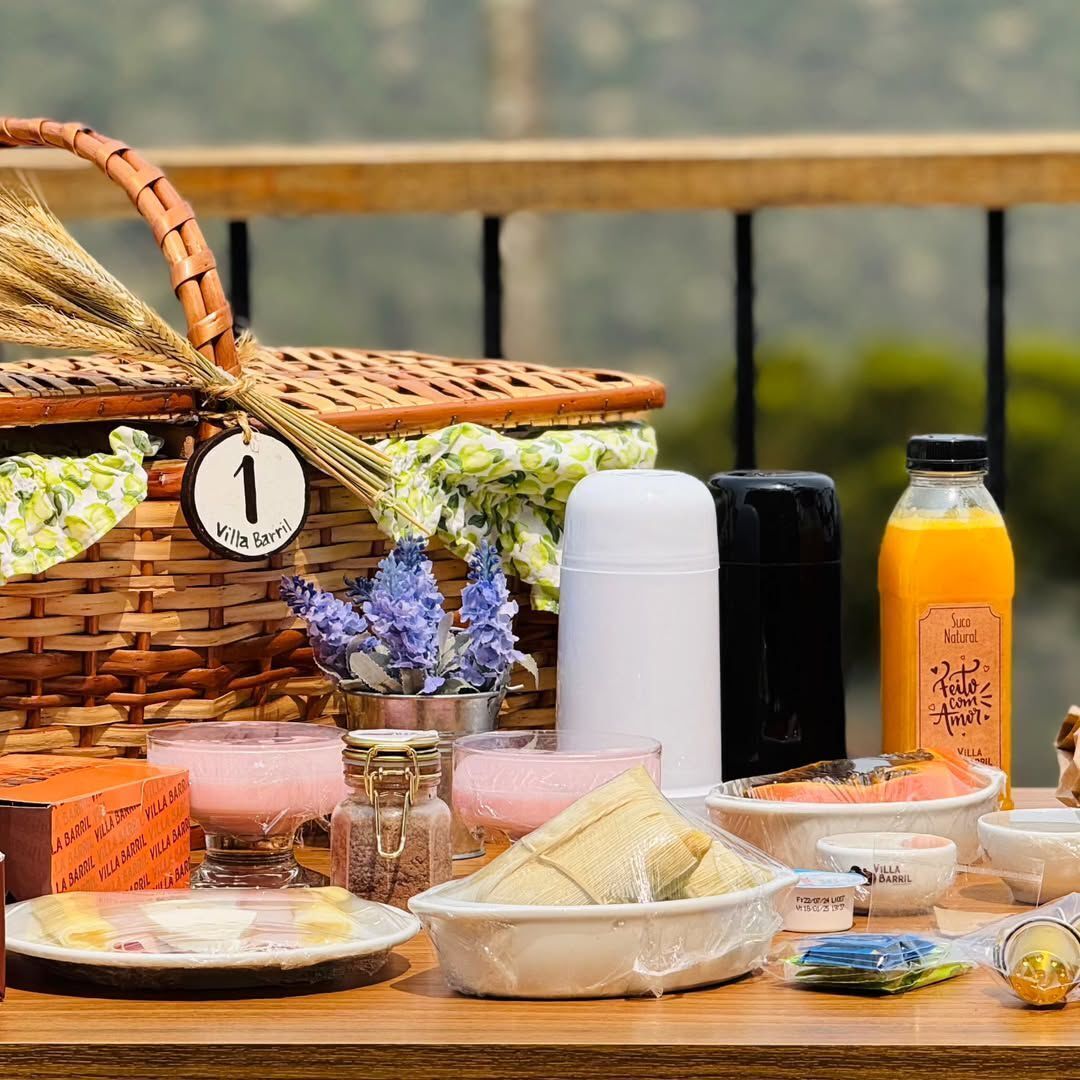 Una disposición para un picnic con una cesta de mimbre, un termo, una botella de jugo y diferentes alimentos sobre una mesa de madera.