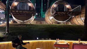 A wooden deck with a fire pit, a musician, and two large, circular wooden structures with railings. - Pousada Villa Barril (Camanducaia)