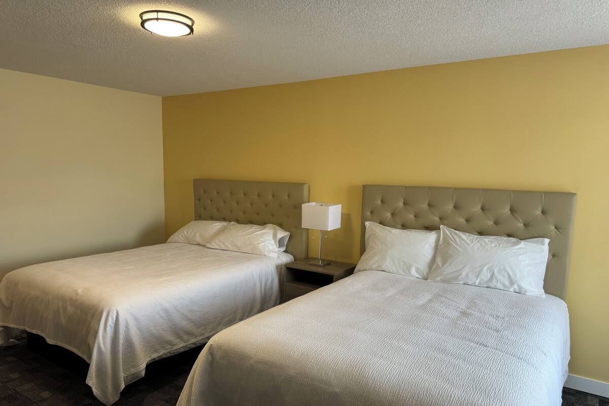 A hotel room with two beds, a nightstand with a lamp, and a ceiling light.