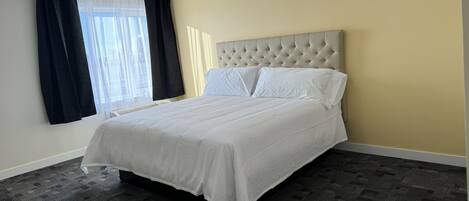 A neatly made bed with white linens in a room with a beige wall and a patterned carpet.