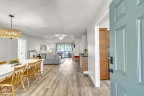 Eine moderne Küche mit Holzausstattung, ein Essbereich mit weißem Tisch und Stühlen sowie ein Wohnzimmer mit Sofa und Fernseher.