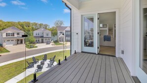 A covered porch with outdoor seating, a view of a residential street, and a sliding glass door leading to an interior space.