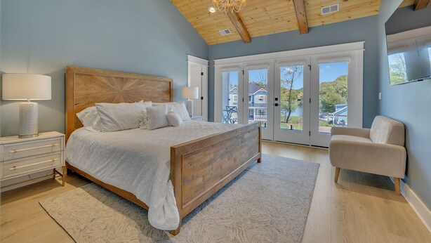 A bedroom with a wooden bed, a nightstand, a chair, and a large window with a view of houses.