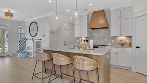 A modern kitchen with a large island, bar stools, white cabinetry, and pendant lighting.
