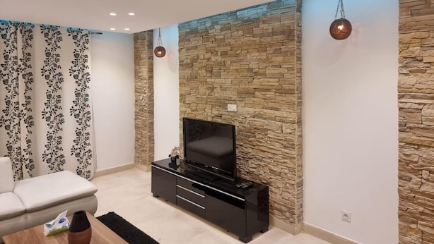 A modern living room with a stone accent wall, a black entertainment unit, and a white sofa. - Rehab City- Appartement Cosy-chic Près de Toutes Commodités (Cairo Governorate)
