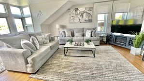 A living room with a grey sofa, a coffee table, and a TV. - Harrisburg apt Great River View (Harrisburg)