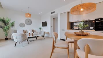 A modern living room with a dining area, featuring a round wooden table, beige chairs, and a hanging light fixture.