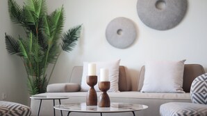 A living room with a sofa, two side tables, a potted plant, and wall decor. - Melior Villas (Preveza)