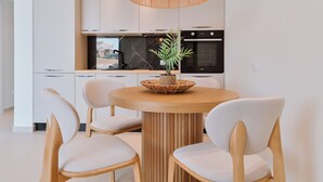 A modern kitchen with white cabinets, a wooden dining table with four chairs, and a hanging light fixture. - Melior Villas (Preveza)