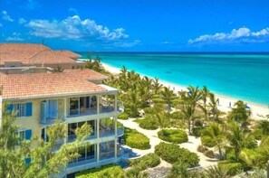 Un edificio de varios pisos con balcones, una playa y palmeras.
