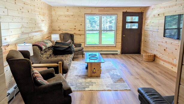 Interior acogedor de una cabaña con paredes de madera, un conjunto de sofás, una mesita y vistas al exterior a través de una ventana.