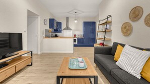 Una sala de estar moderna con televisor, sofá, mesa de centro y una cocina al fondo.