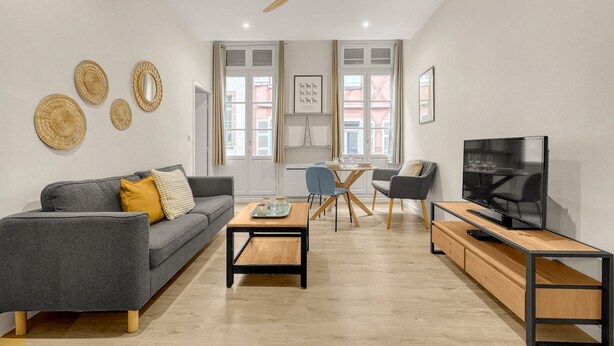 Una sala de estar moderna con un sofá gris, una mesa de centro de madera, un televisor sobre un mueble de madera y un ventilador de techo.