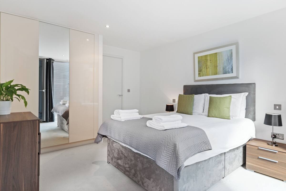 A modern bedroom with a bed, bedside tables, a wardrobe, and a mirror.