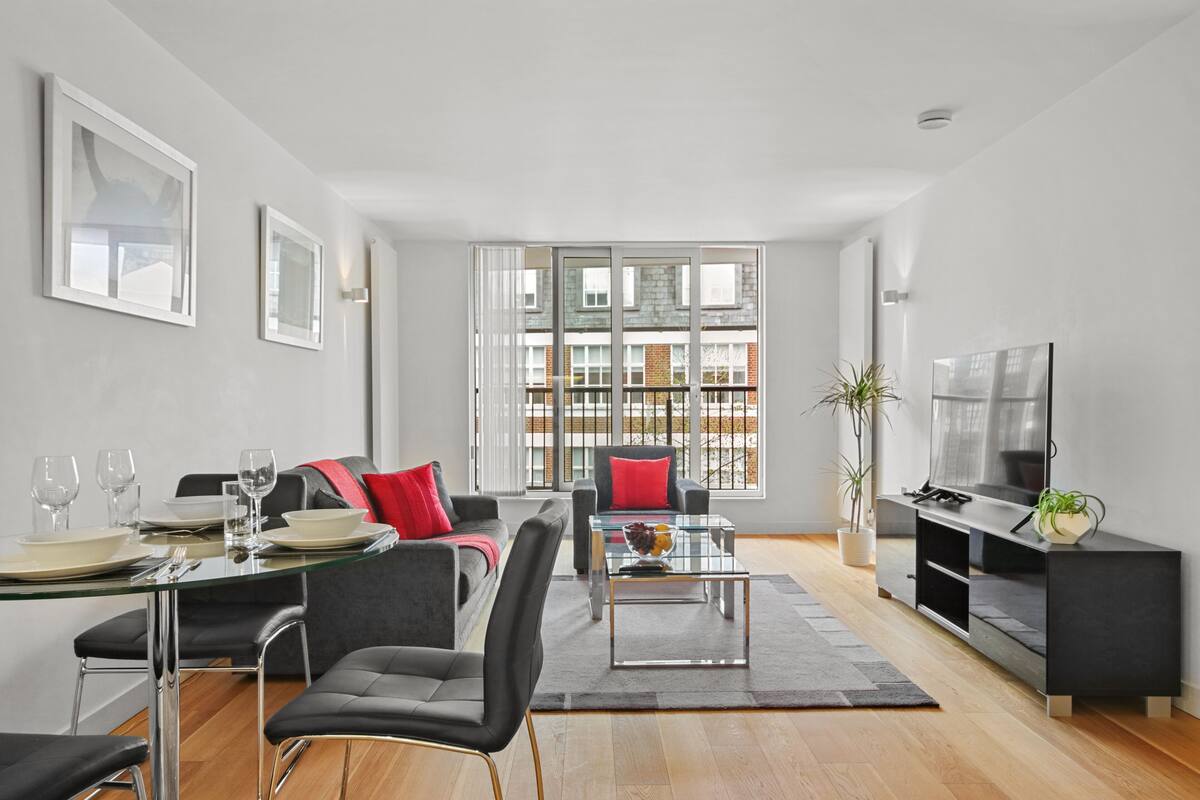 A modern living room with a dining area, large windows, and a flat-screen TV.