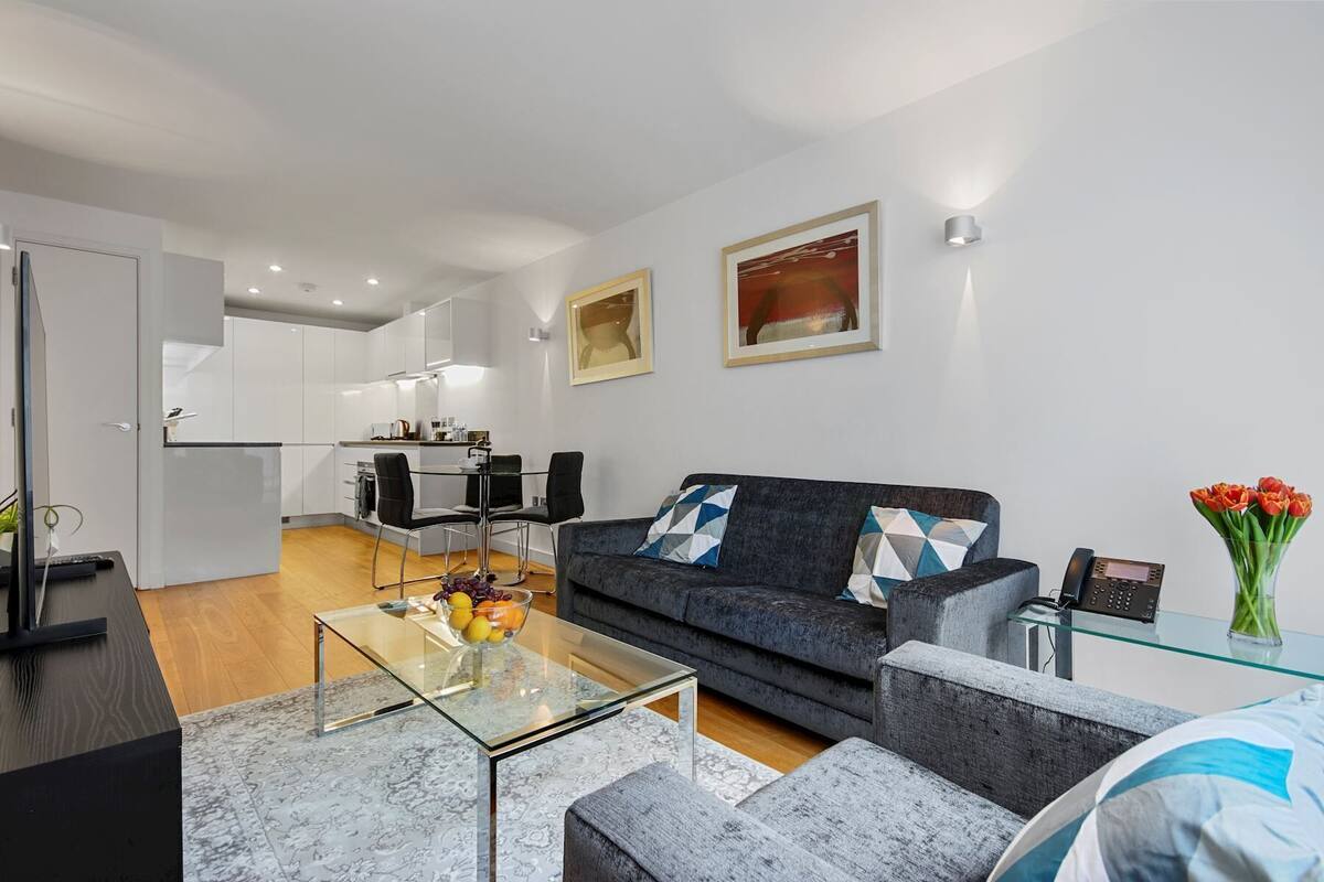 A modern living room with a glass coffee table, grey sofa, and a dining area with a glass table and chairs.