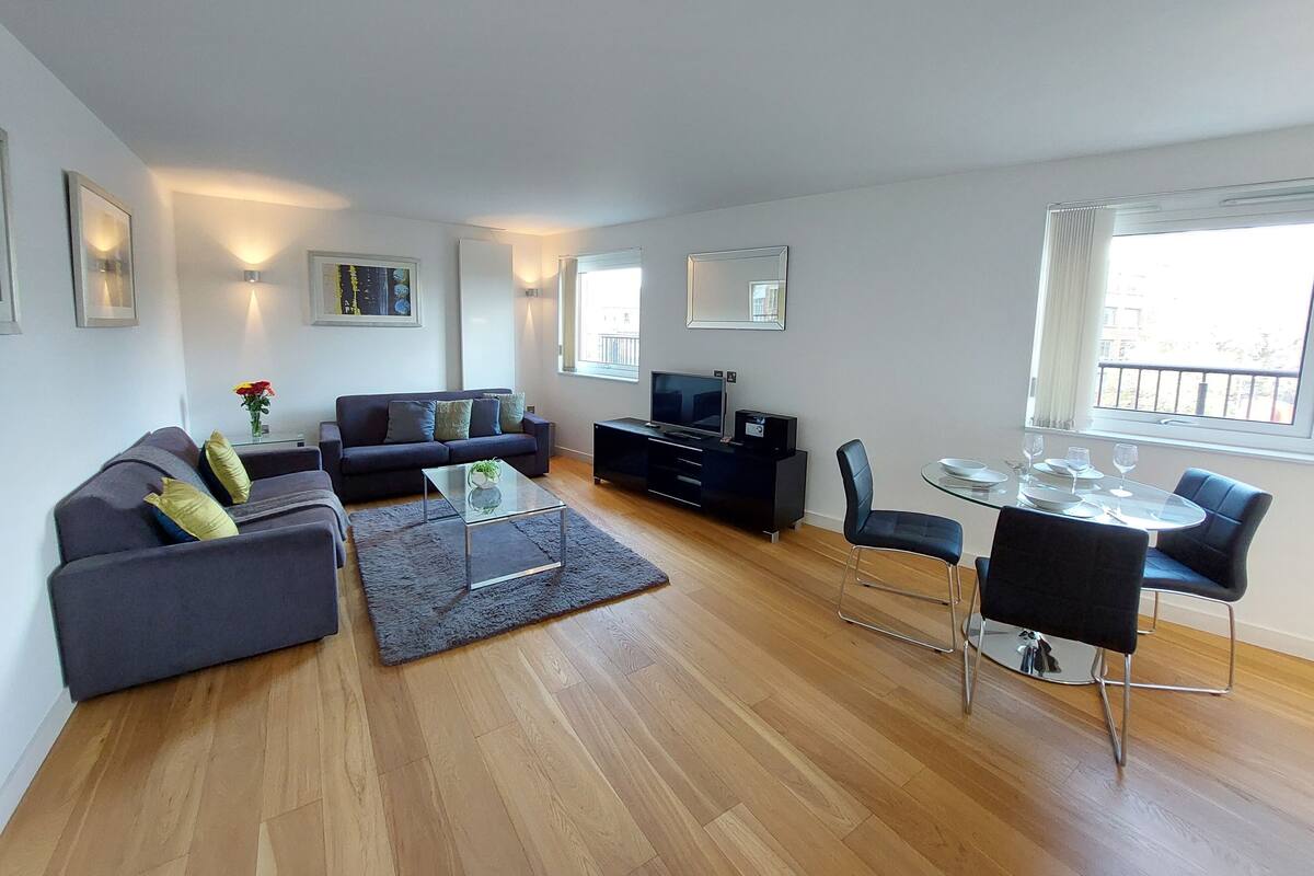 A modern living room with a sofa, coffee table, TV, and dining area with chairs and a glass table.