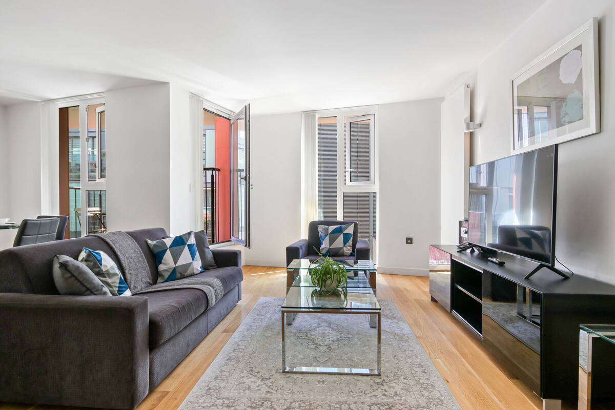 A modern living room with a grey sofa, a glass coffee table, and a flat-screen TV.