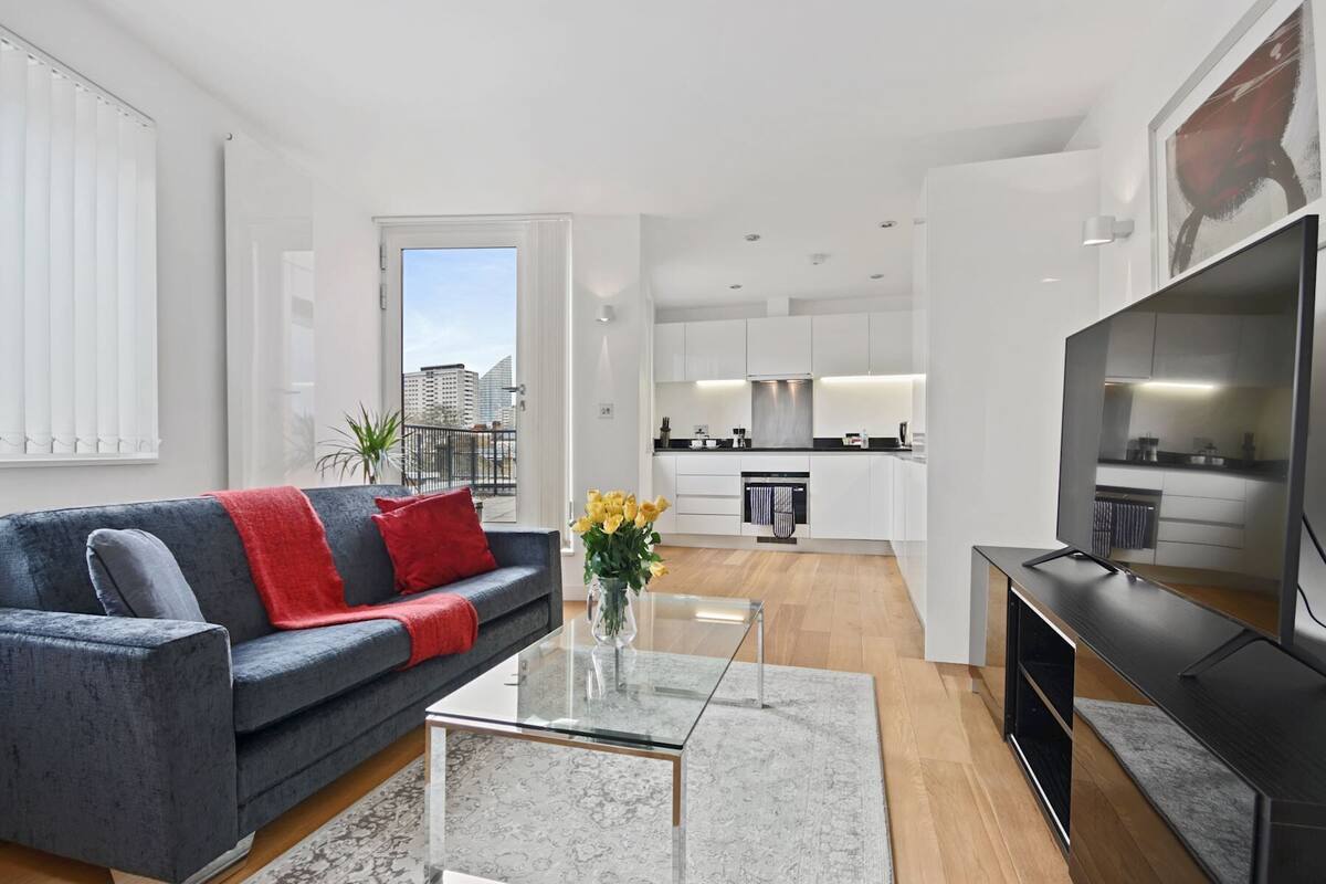 A modern living room with a grey sofa, a glass coffee table, and a TV stand.