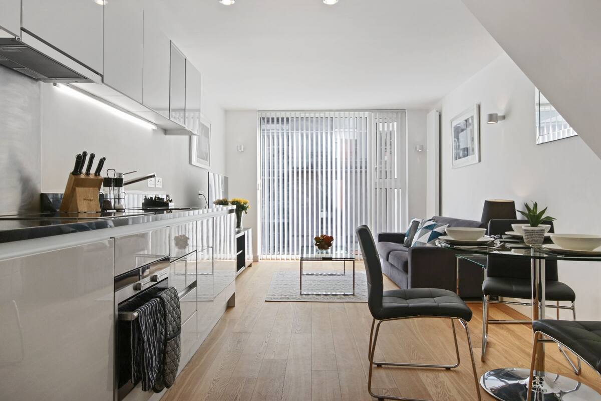 A modern kitchen with a glass dining table, black chairs, and a grey sofa.