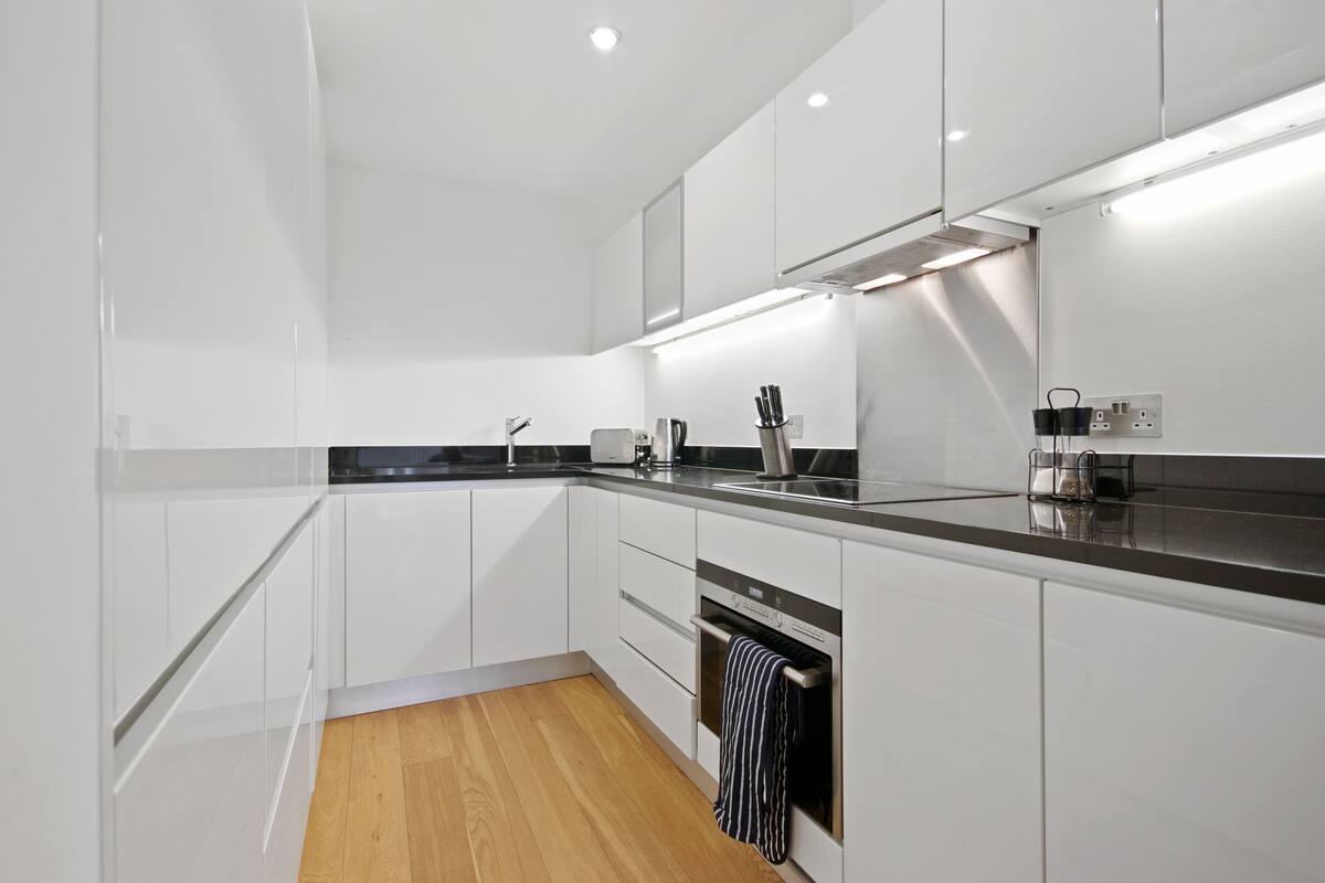 A modern kitchen with white cabinets, a black countertop, and a wooden floor.