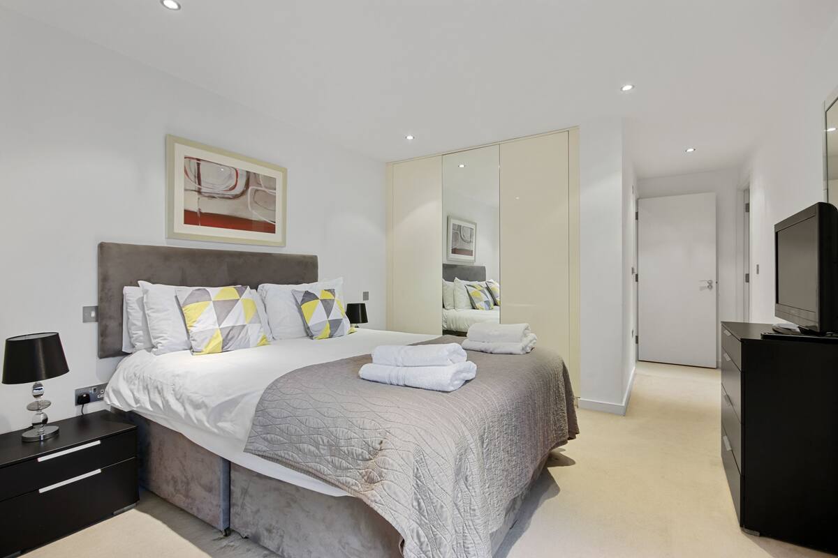 A modern bedroom with a large bed, bedside tables, a mirror, and a TV.