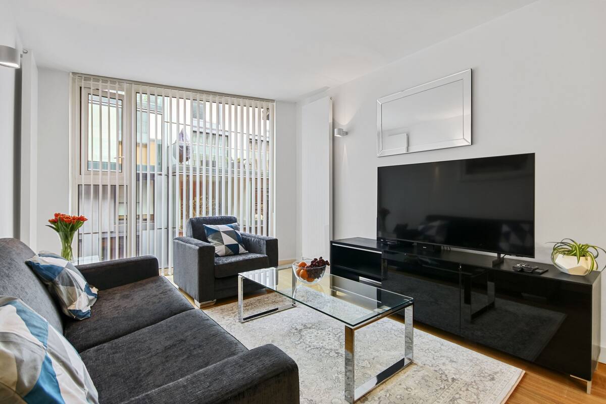 A modern living room with a sofa, armchair, glass coffee table, and a flat-screen TV on a black stand.