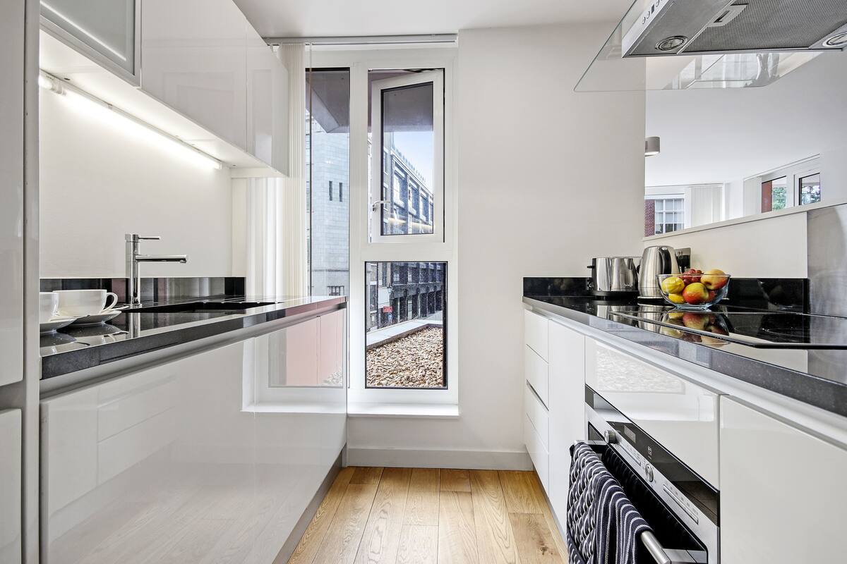 A modern kitchen with a large window, white cabinetry, and a black countertop.