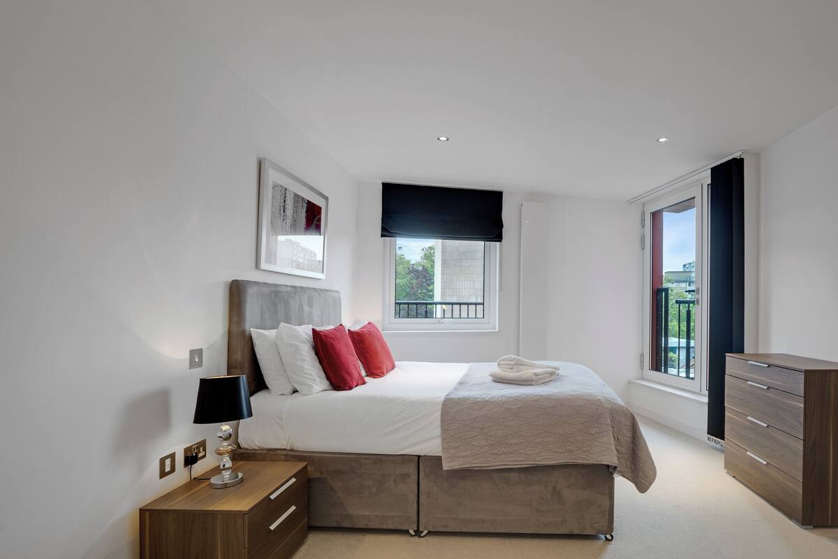 A modern bedroom with a bed, bedside table, and a window with a view.