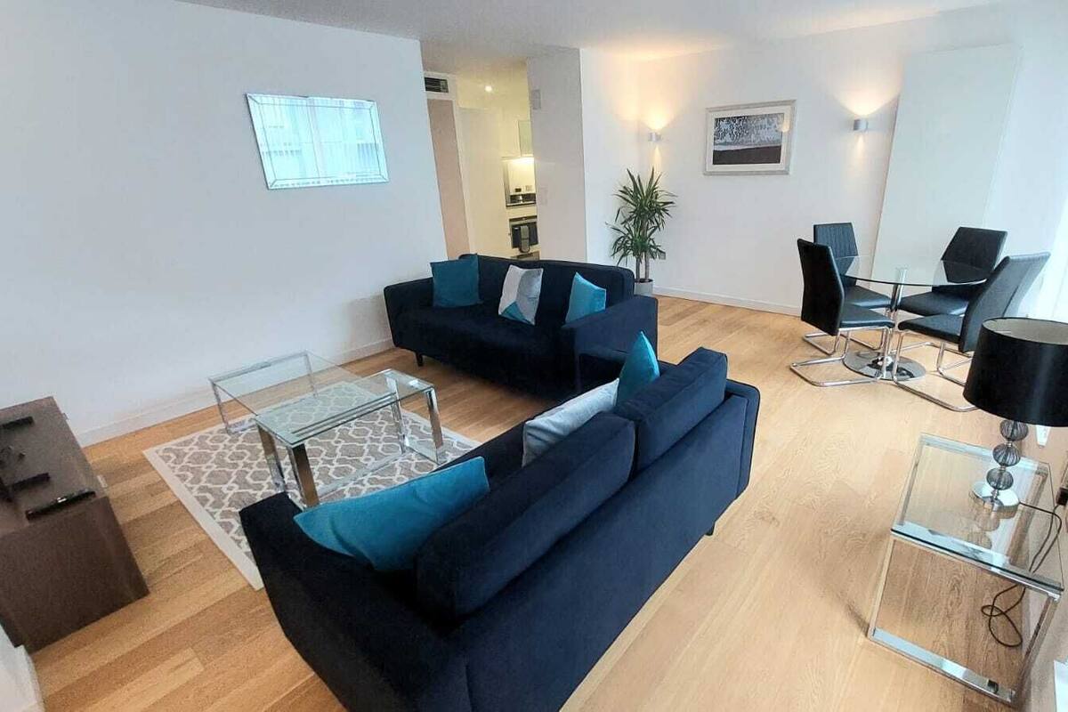 A modern living room with two dark sofas, a glass coffee table, and a dining area with chairs and a lamp.