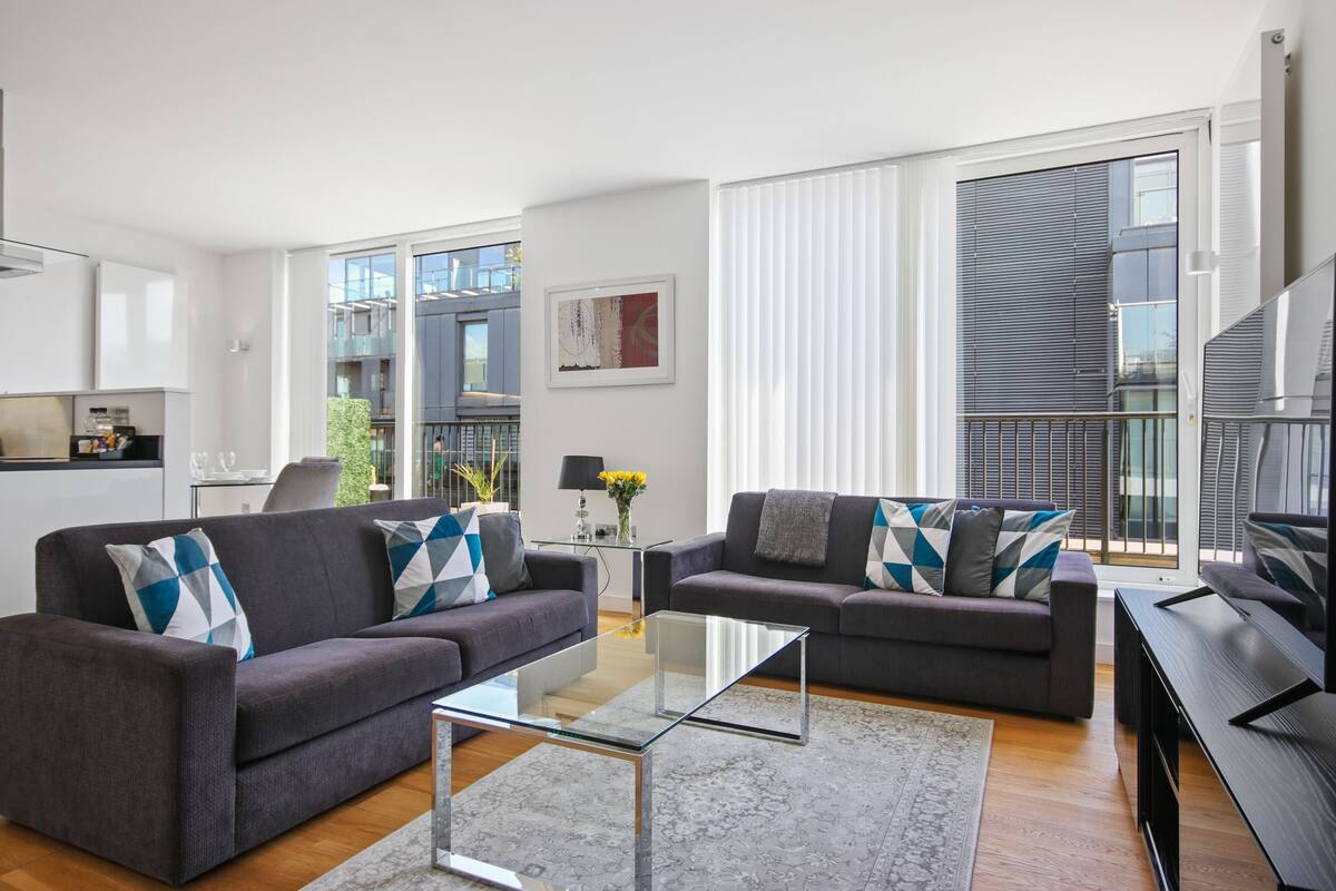 A modern living room with two grey sofas, a glass coffee table, and a flat-screen TV.