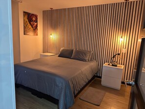 Ein Schlafzimmer mit einem Bett, Nachttischen, einer Lampe, einer Wandleuchte und einem Gemälde.