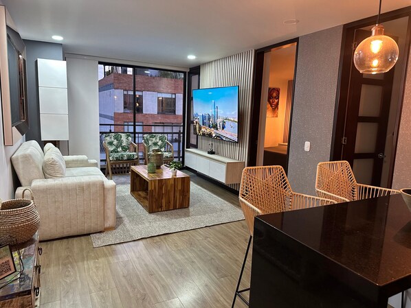 Ein modernes Wohnzimmer mit einer Couch, Sesseln, einem Couchtisch, einem Fernseher und einem Balkon mit Blick auf die Stadt.