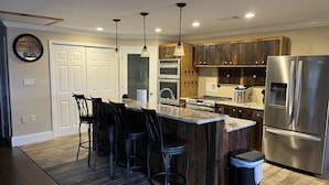 A modern kitchen with a central island, bar stools, stainless steel appliances, and wooden cabinetry.