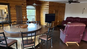 A log cabin interior with a dining table, chairs, a television, and a leather sofa.