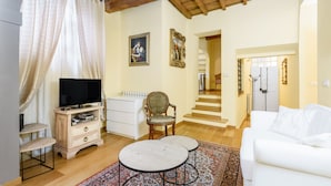A living room with a television, white sofa, wooden floor, and a patterned rug. - Il Nido di Santa Croce by Mmega (Florence)