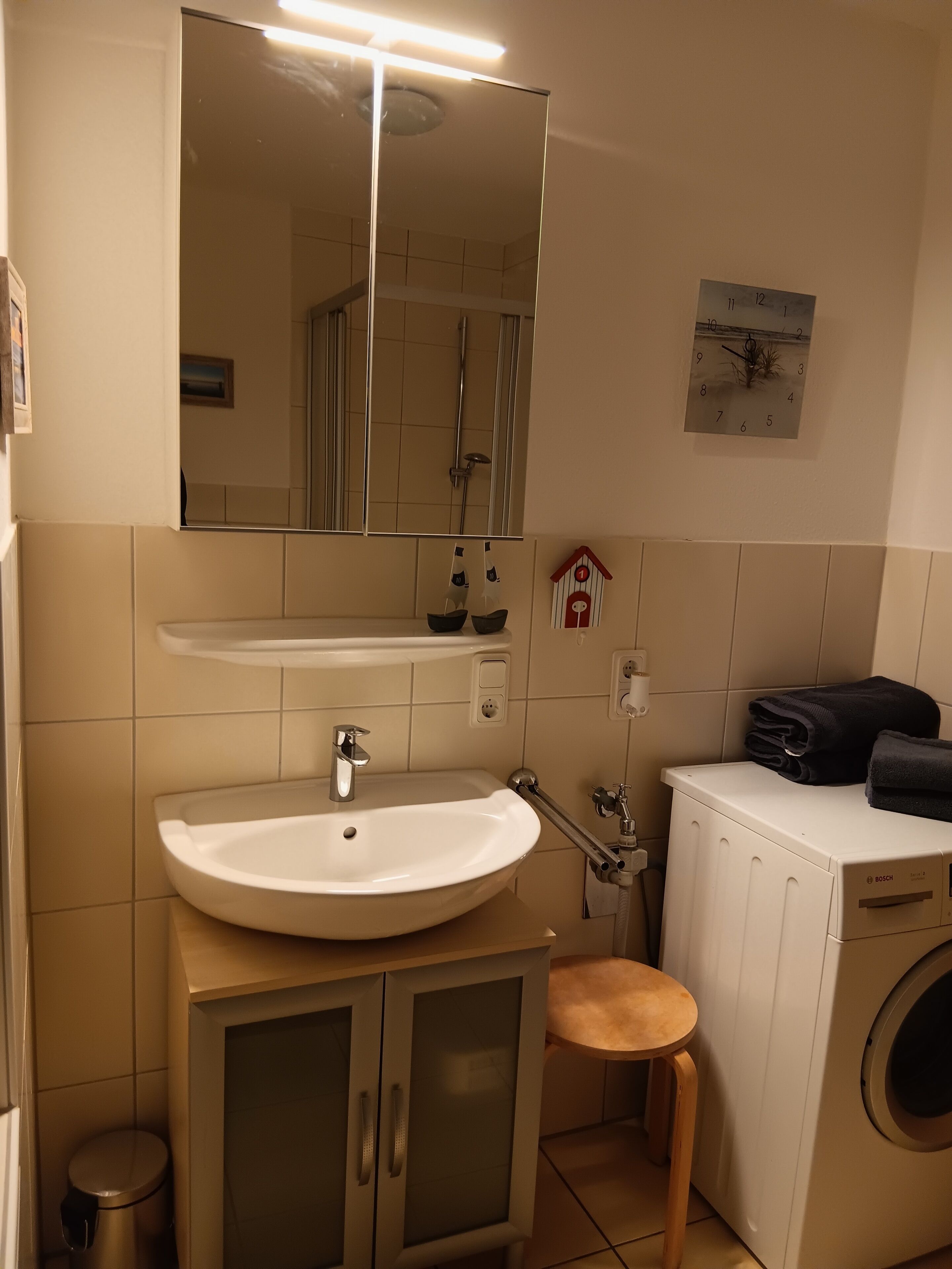 A bathroom with a sink, mirror, towel rack, clock, and a washing machine.