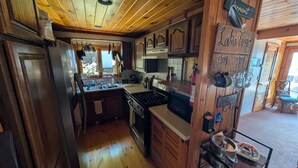 A kitchen with wooden cabinets, a stove, and a sink. - Lake Champlain house: sunsets, mountains, fishing (Georgia)