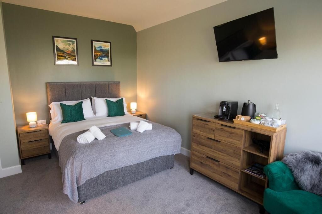 A bedroom with a bed, bedside tables, a TV, a dresser, and artwork on the wall.
