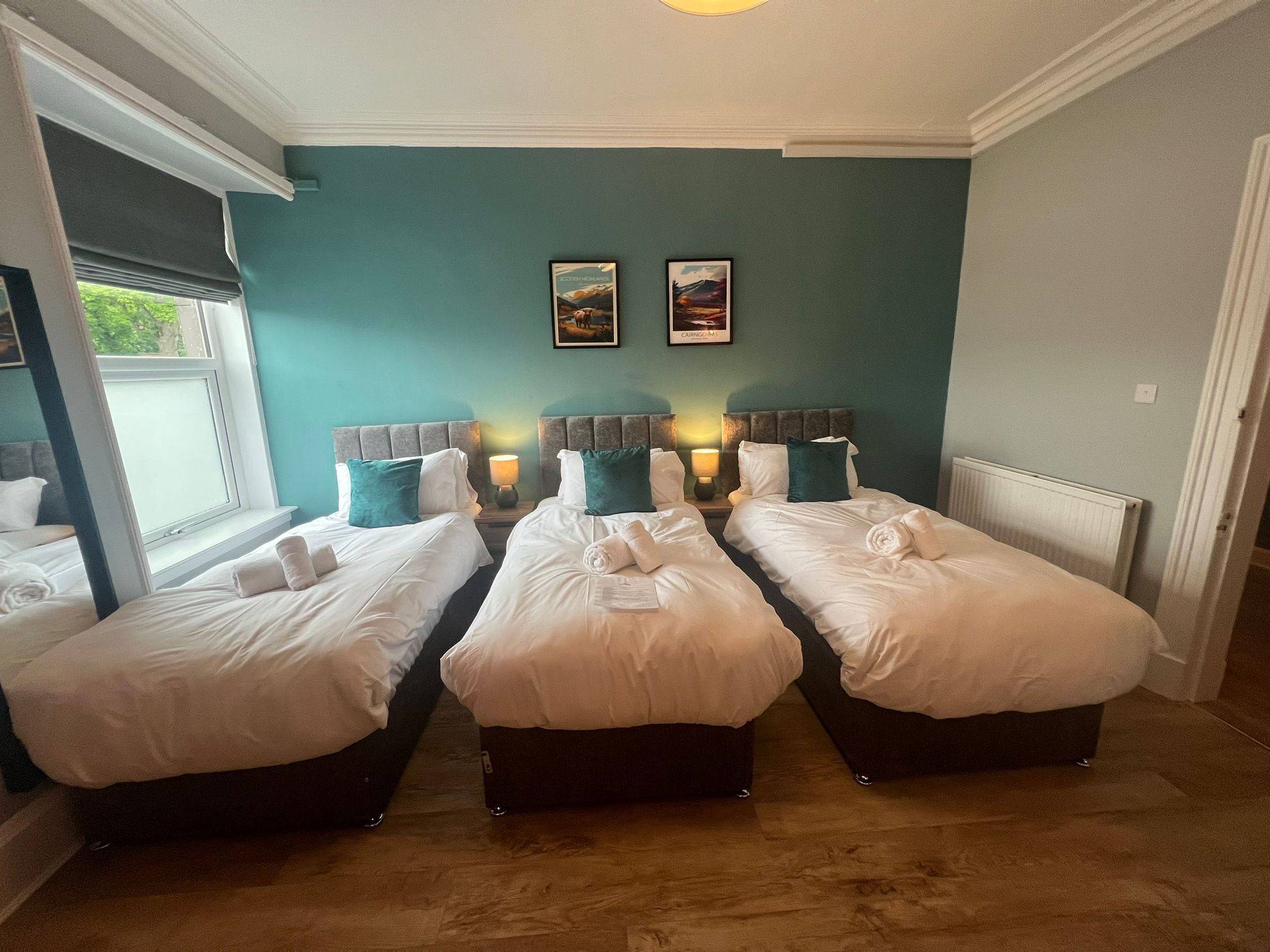 A hotel room with two single beds, a window with a view, and two wall-mounted lamps.