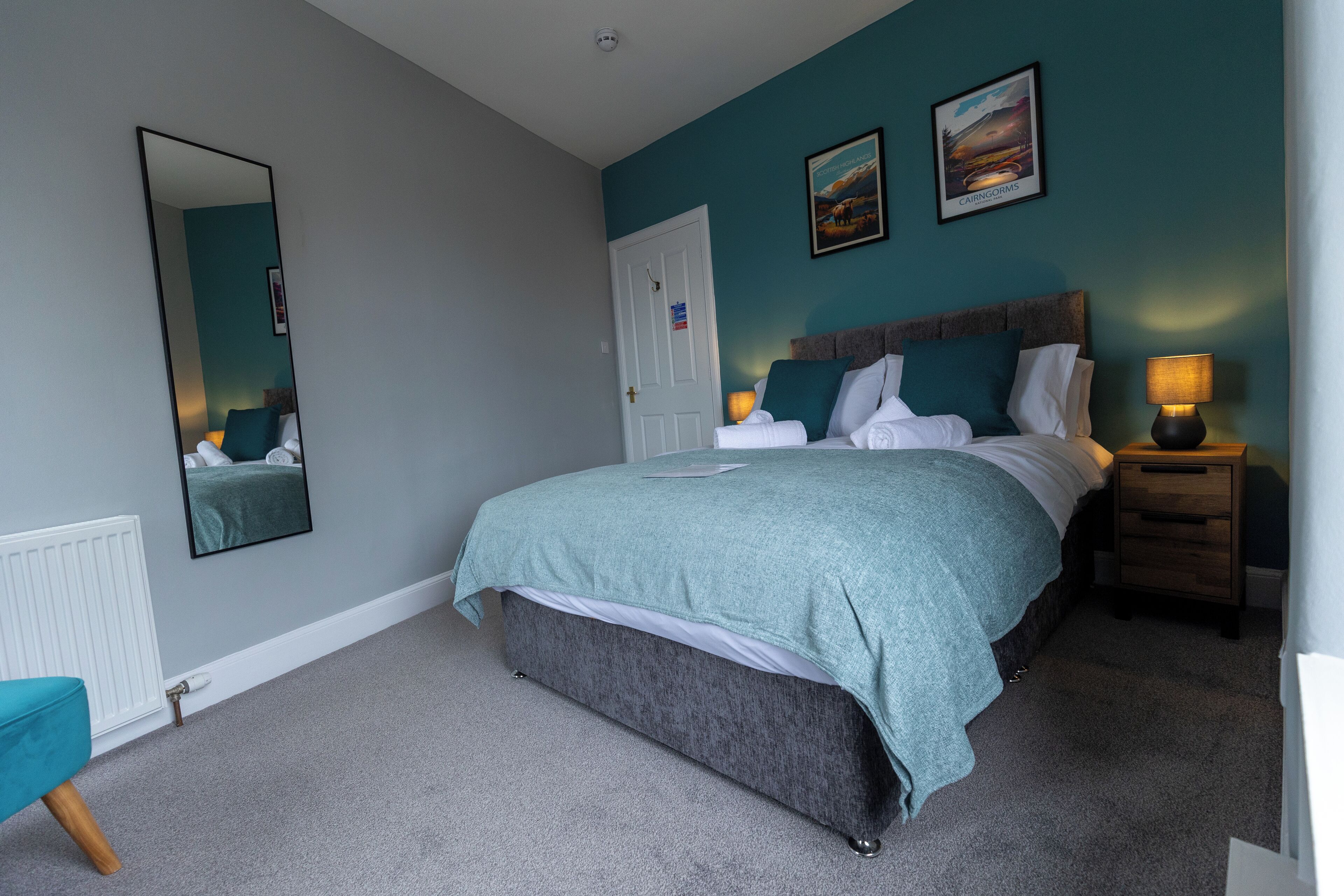 A bedroom with a bed, a bedside table with a lamp, a mirror, and a picture on the wall.