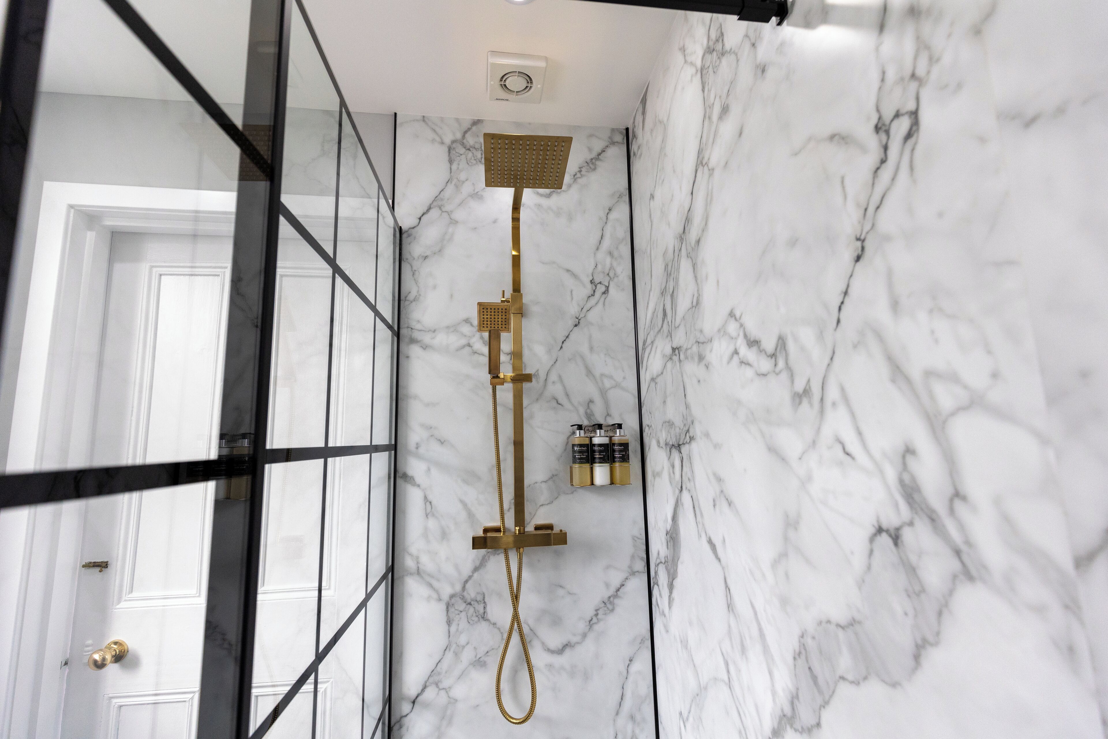 A modern bathroom with a marble wall, a shower with a gold fixture, and a door with a brass handle.