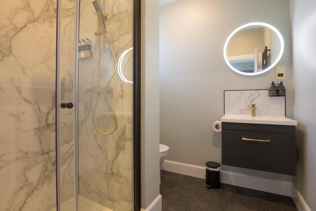 Un baño con cabina de ducha de vidrio, pared de mármol, lavabo con espejo e inodoro.