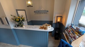 A reception area with a blue counter, a sign reading "The Crossing," a vase with flowers, and a window with a view. - The Crossing (Kingussie)