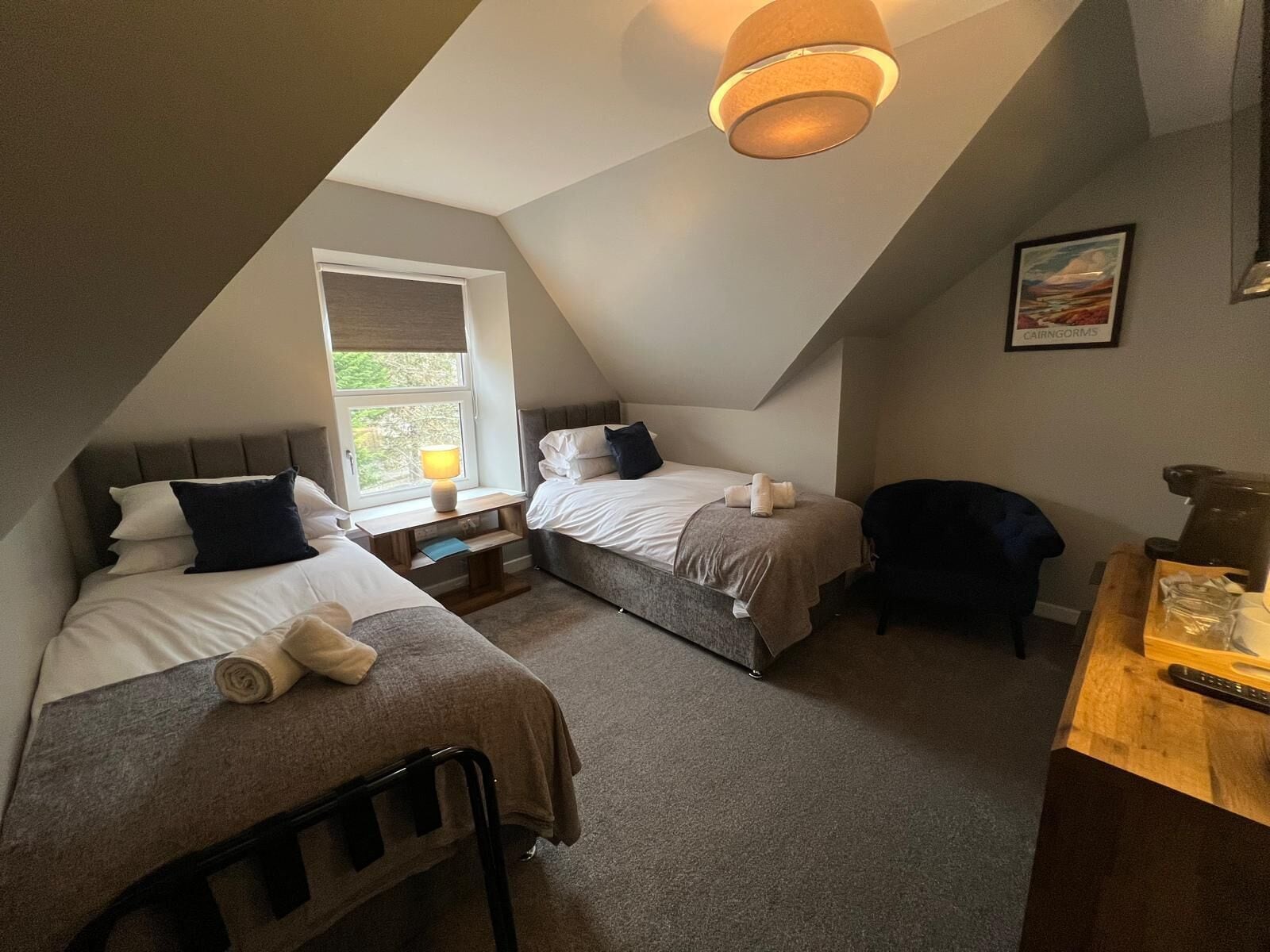 A cozy attic bedroom with two beds, a window, and a ceiling light.