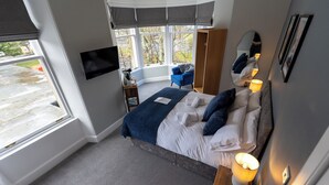 A bedroom with a bed, bedside lamps, a TV, a chair, and a wardrobe. - The Crossing (Kingussie)