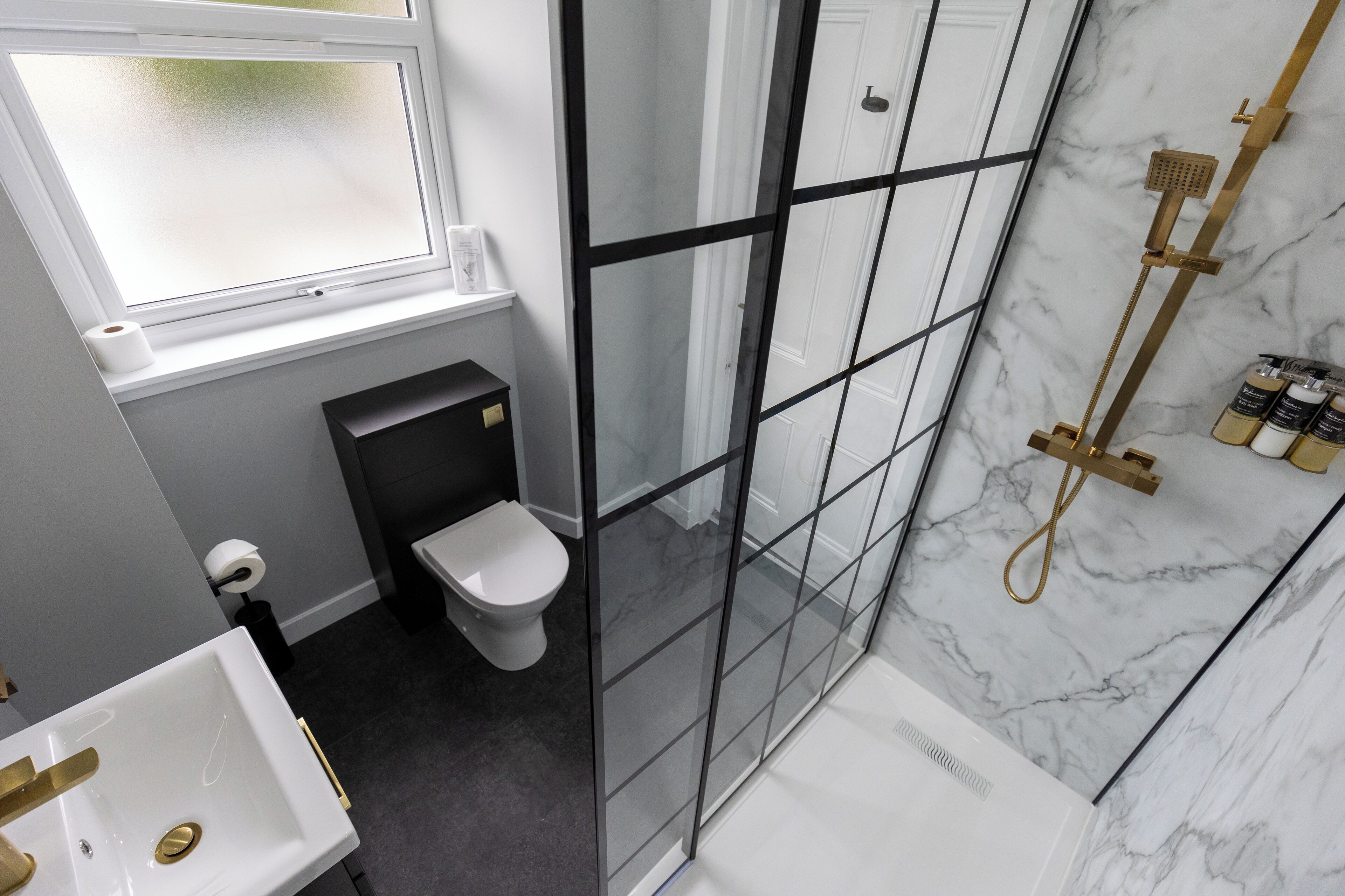 A modern bathroom with a glass shower enclosure, a white toilet, and a sink with gold fixtures.